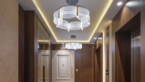 Un couloir moderne avec un sol en marbre, des portes en bois et un lustre central.