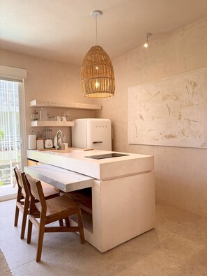 A modern kitchen with a central island, white cabinetry, and a hanging rattan light fixture.