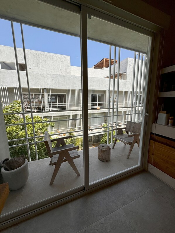 A balcony with a view of a building, a wooden chair, a small wooden stool, and a potted plant. - Jungle Chic Suites by Marea (Tulum)