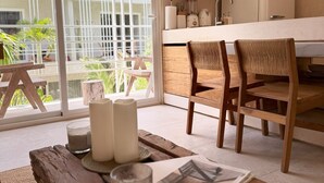 A modern kitchen with a white countertop, wooden chairs, and a large window with a view of greenery. - Jungle Chic Suites by Marea (Tulum)