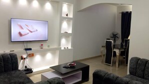 A modern living room with a flat-screen TV, dark sofas, a coffee table, and built-in shelving with decorative items.
