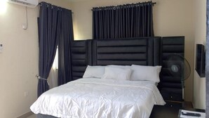 A bedroom with a bed, dark curtains, a ceiling fan, and an air conditioning unit.