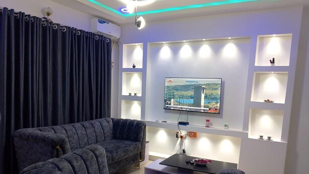A modern living room with a sectional sofa, a flat-screen TV mounted on the wall, and built-in shelves.
