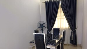 A room with a dining table, chairs, a fan, and black curtains.