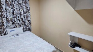 Un dormitorio con cama, almohada con logotipo, cortina estampada y estantería blanca.