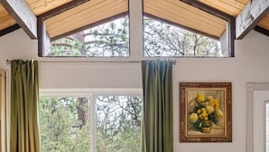 Amplia sala de estar con techo alto, ventanas grandes, un sofá, una mesa de centro y un cuadro en la pared.