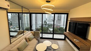 A modern living room with a sofa, two small tables, a TV, and a city view through large windows. - Cozy studio in Panama City (Panamá)