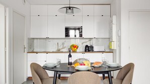 A modern kitchen with white cabinets, a marble countertop, and a dining area with a round table and four chairs. - TBS 140 - Elegantly decorated apartment (Paris)