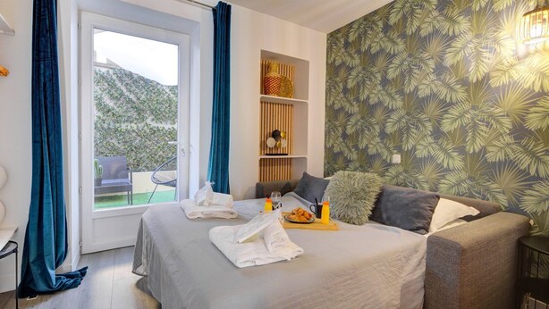 Quarto com cama, sofá, pequena mesa com itens de café da manhã, prateleira com objetos decorativos e vista para o verde lá fora.