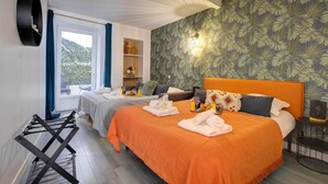 Quarto de hotel com duas camas, varanda, janela grande e parede com padrão de folhagem tropical.