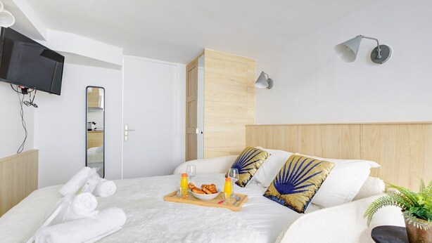A hotel room with a bed, a bedside table with a plant, a flat-screen TV mounted on the wall, and a wooden wardrobe. - TheBlueStay 72 - Cozy Studio - Marais District (Paris)