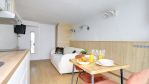 A modern kitchen with a wooden countertop, a dining table with breakfast items, a white sofa, and a TV mounted on the wall. - TheBlueStay 72 - Cozy Studio - Marais District (Paris)