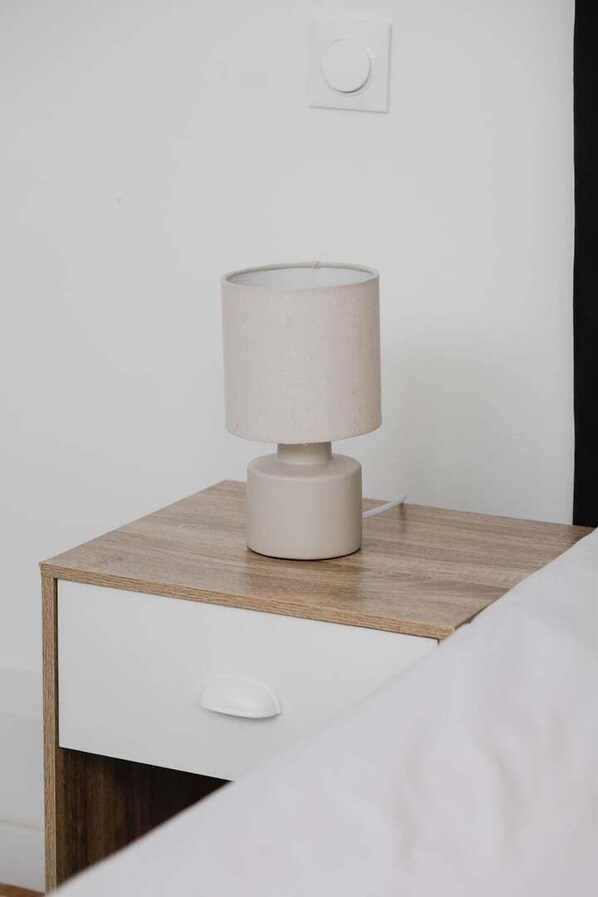 A simple bedside table with a lamp, a drawer, and a power outlet on the wall.