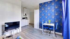 Una sala de estar moderna con un televisor de pantalla plana, un comedor con mesa y sillas, y una cocina al fondo.