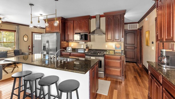 A modern kitchen with dark wood cabinets, stainless steel appliances, and a granite island with bar stools. - Lake View Condo - Walk to Saugatuck (Douglas)