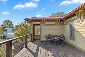 A wooden deck with a table and chairs, a metal railing, and a door leading to a covered area. - Lake View Condo - Walk to Saugatuck (Douglas)