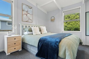 A bedroom with a bed, a nightstand, a dresser, a window with a view of trees, and a wall-mounted light fixture. - No longer active (Martinborough)