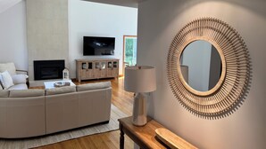 A modern living room with a large TV, a sofa, a wooden cabinet, and a unique circular mirror. - HarwichPort 4 bdr 3 bath - Walk to Red River Beach - next to Wychmere (Harwich)