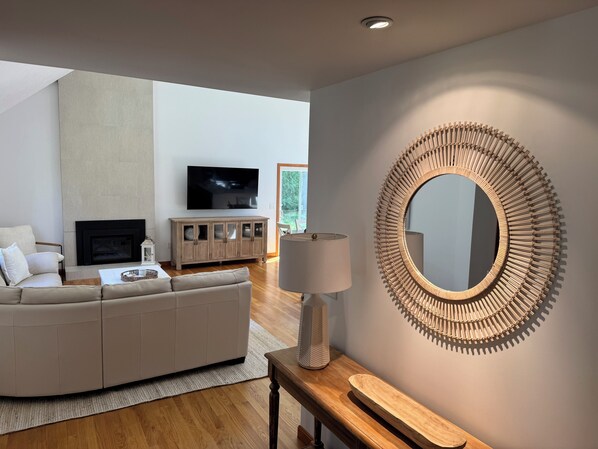 A modern living room with a large TV, a sofa, a wooden cabinet, and a unique circular mirror.