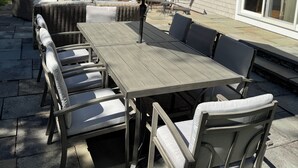 An outdoor patio with a wooden table and chairs, a large umbrella, and a house in the background. - HarwichPort 4 bdr 3 bath - Walk to Red River Beach - next to Wychmere (Harwich)