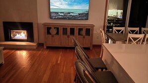 A living room with a fireplace, a television mounted on the wall, and a dining area with chairs. - HarwichPort 4 bdr 3 bath - Walk to Red River Beach - next to Wychmere (Harwich)