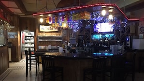 A bar area with a counter, bar stools, shelves with bottles, and a patterned floor.