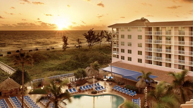 A hotel with a pool, lounge chairs, and a view of the ocean at sunset.