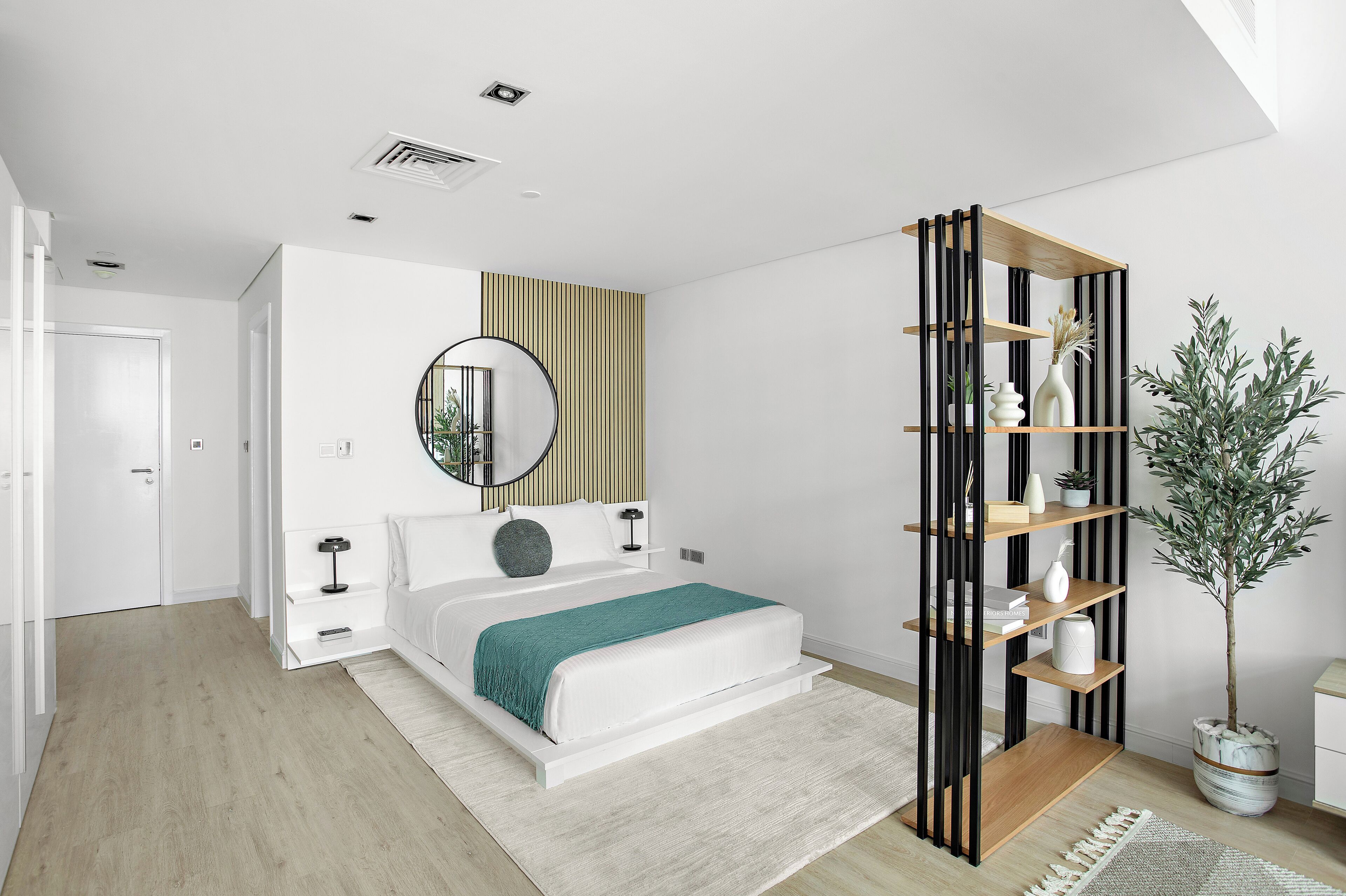 A modern bedroom with a bed, bedside tables, a mirror, and a built-in shelving unit with decorative items.