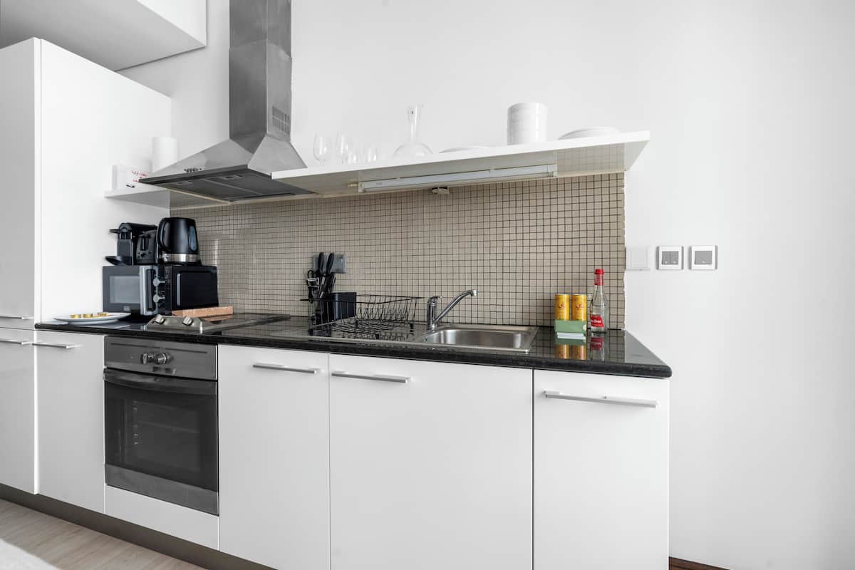 A modern kitchen with white cabinets, a black countertop, a stainless steel sink, and a built-in oven.