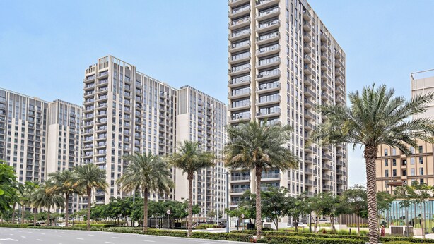 Un immeuble résidentiel de grande hauteur, doté de nombreux balcons, entouré de palmiers et agrémenté d’un aménagement paysager soigné.