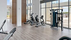 Une salle de sport moderne dotée de grandes fenêtres, d’équipements d’exercice et d’un plancher en bois.