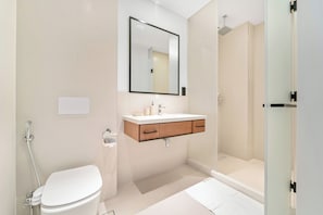 A modern bathroom with a toilet, sink, mirror, and shower.