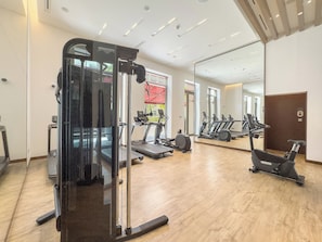 A gym with exercise equipment, a mirror, and a wooden floor.