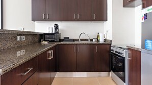 Una cocina moderna con armarios de madera oscura, encimeras de granito, horno empotrado y refrigerador de acero inoxidable.