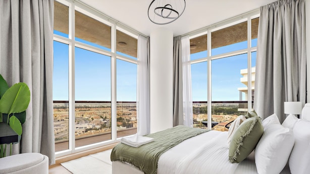 Un dormitorio con una cama grande, vistas a un paisaje urbano y una lámpara de araña moderna.