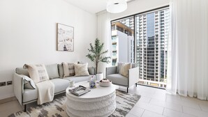 A modern living room with a sofa set, a coffee table, and a large window with a view of a high-rise building. - Silkhaus Sobha Hartland Greens (Dubai)