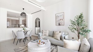 A modern living room with a round coffee table, grey sofa, and a dining area with chairs. - Silkhaus Sobha Hartland Greens (Dubai)