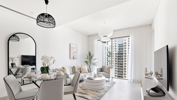 A modern living room with a dining area, large windows, and a flat-screen TV. - Silkhaus Sobha Hartland Greens (Dubai)