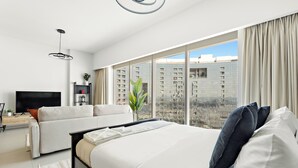 Une chambre d’hôtel moderne dotée d’un grand lit, d’un canapé, d’une télévision et offrant une vue sur la ville grâce à de grandes fenêtres du sol au plafond.