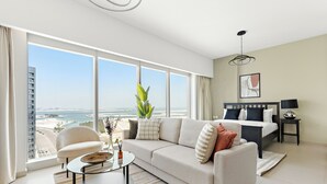 Un salon moderne doté d’une grande fenêtre, d’un canapé, d’une table basse et offrant une vue sur la plage et le paysage urbain.