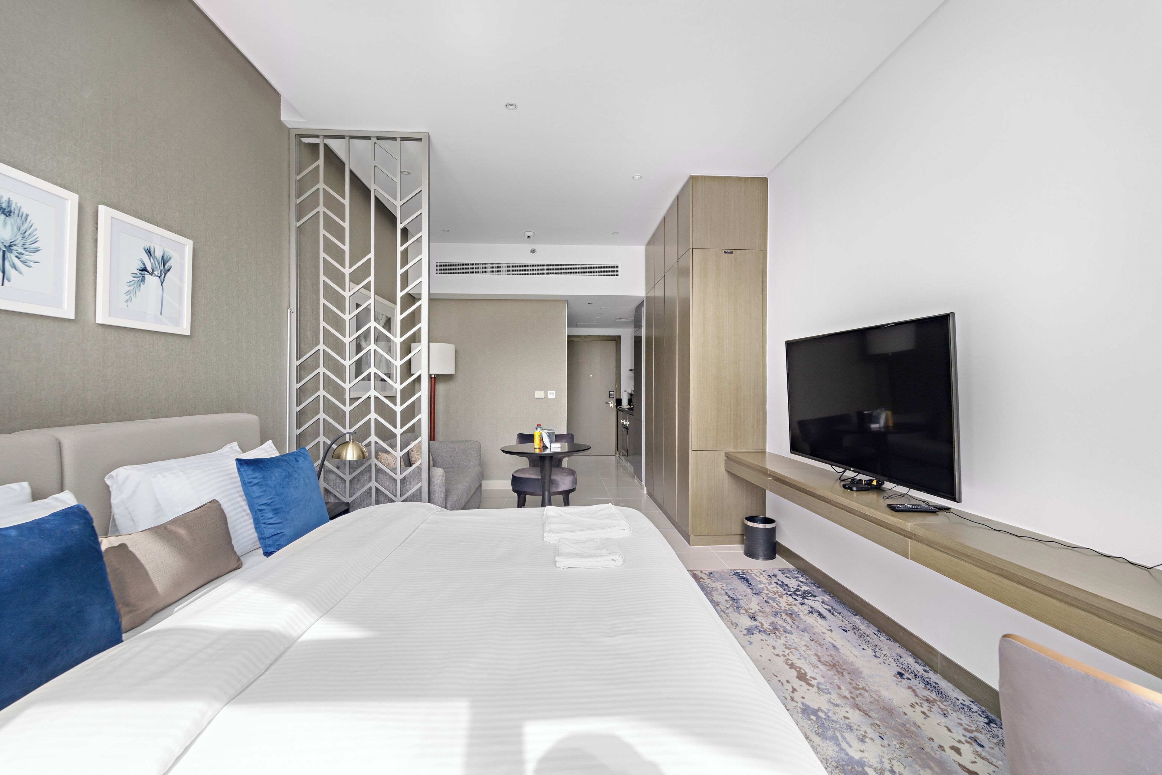 Een moderne hotelkamer met een groot bed, een aan de muur bevestigde televisie en een aparte zithoek met een tafel en stoelen.
