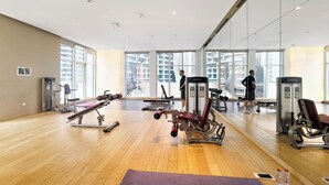 A gym with exercise equipment, large windows, and a wooden floor. - Silkhaus Damac Prive Tower (Dubai)