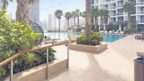 A rooftop pool area with lounge chairs, palm trees, and a view of high-rise buildings. - Silkhaus Damac Prive Tower (Dubai)