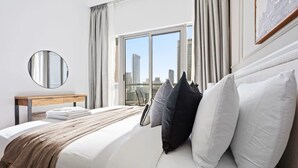 Ein Hotelzimmer mit einem großen Bett, einem runden Spiegel, einem Nachttisch aus Holz und Blick auf die Stadt durch ein großes Fenster.