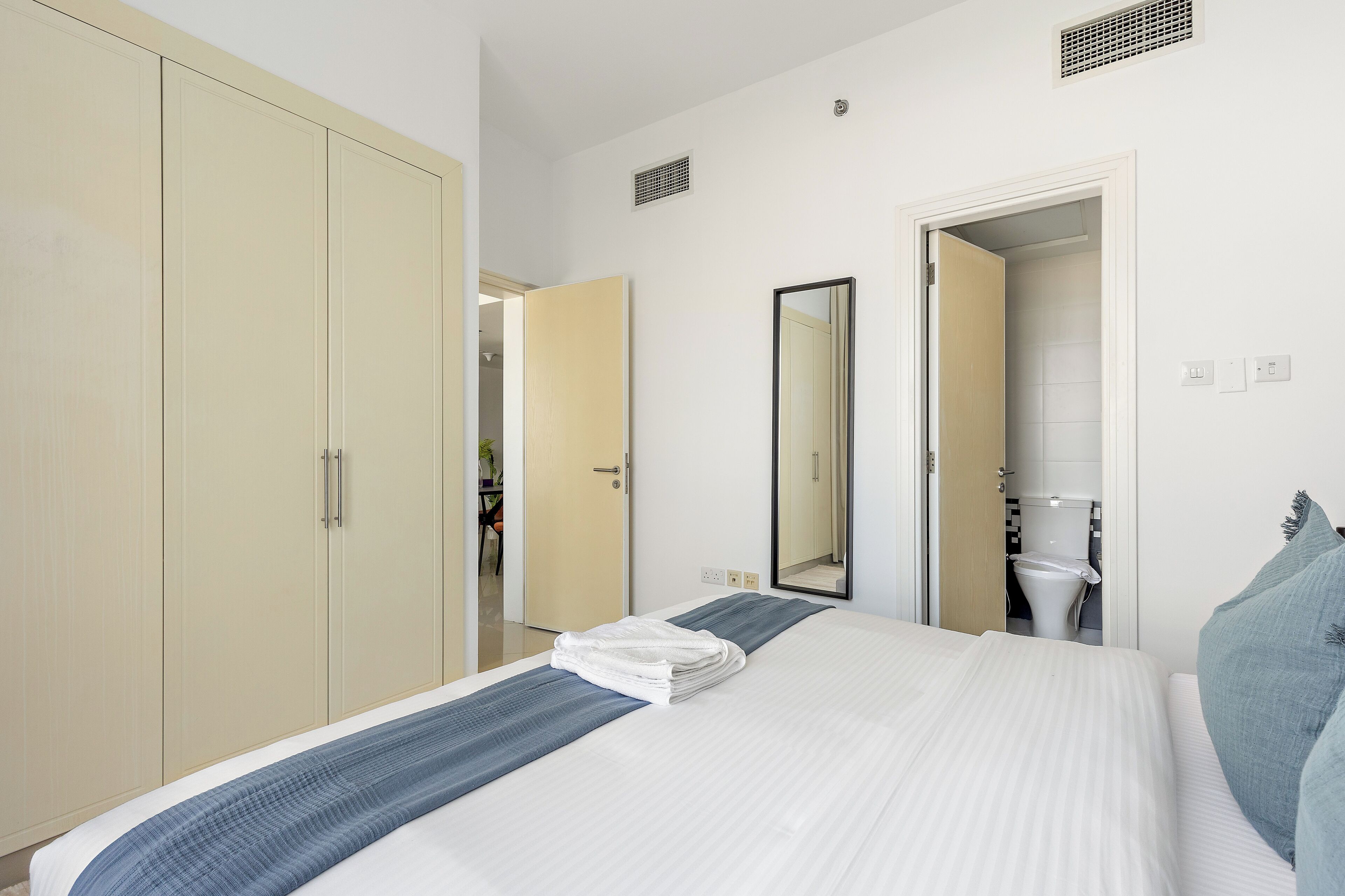 Une chambre d’hôtel comprenant un lit, une armoire, un miroir et une porte ouverte donnant sur une salle de bain.