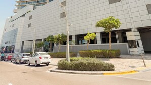 A modern hotel with a curved facade, multiple balconies, and a parking area with cars. - Silkhaus Oceanscape (Abu Dhabi)