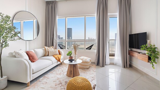 A modern living room with a white sofa, a round coffee table, a TV, and a large window with curtains. - Silkhaus Oceanscape (Abu Dhabi)