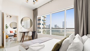 A modern hotel room with a large bed, a desk, a chair, and a view of the cityscape through large windows. - Silkhaus Oceanscape (Abu Dhabi)