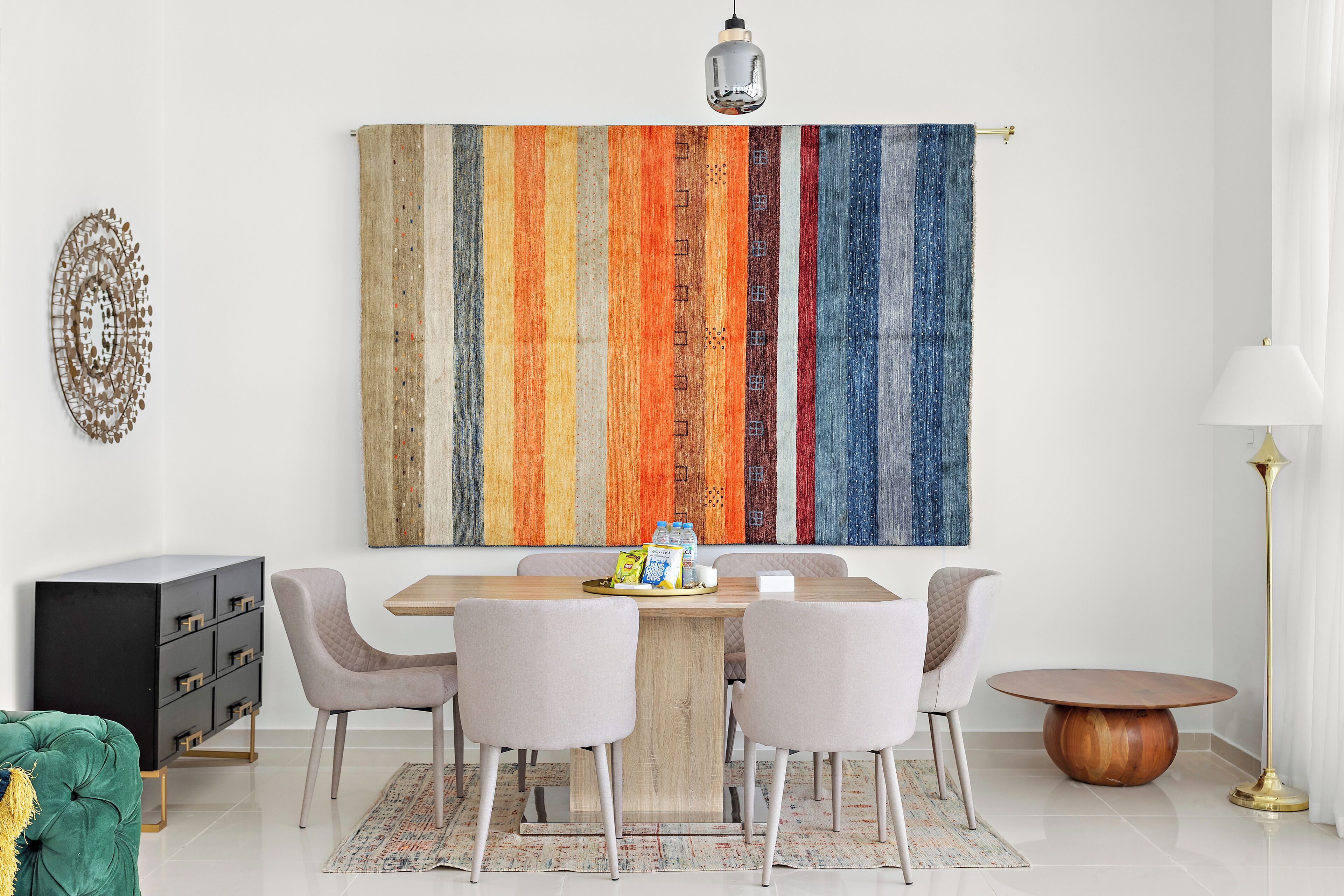 A dining area with a wooden table, four chairs, a black cabinet, a colorful abstract painting, and a floor lamp.