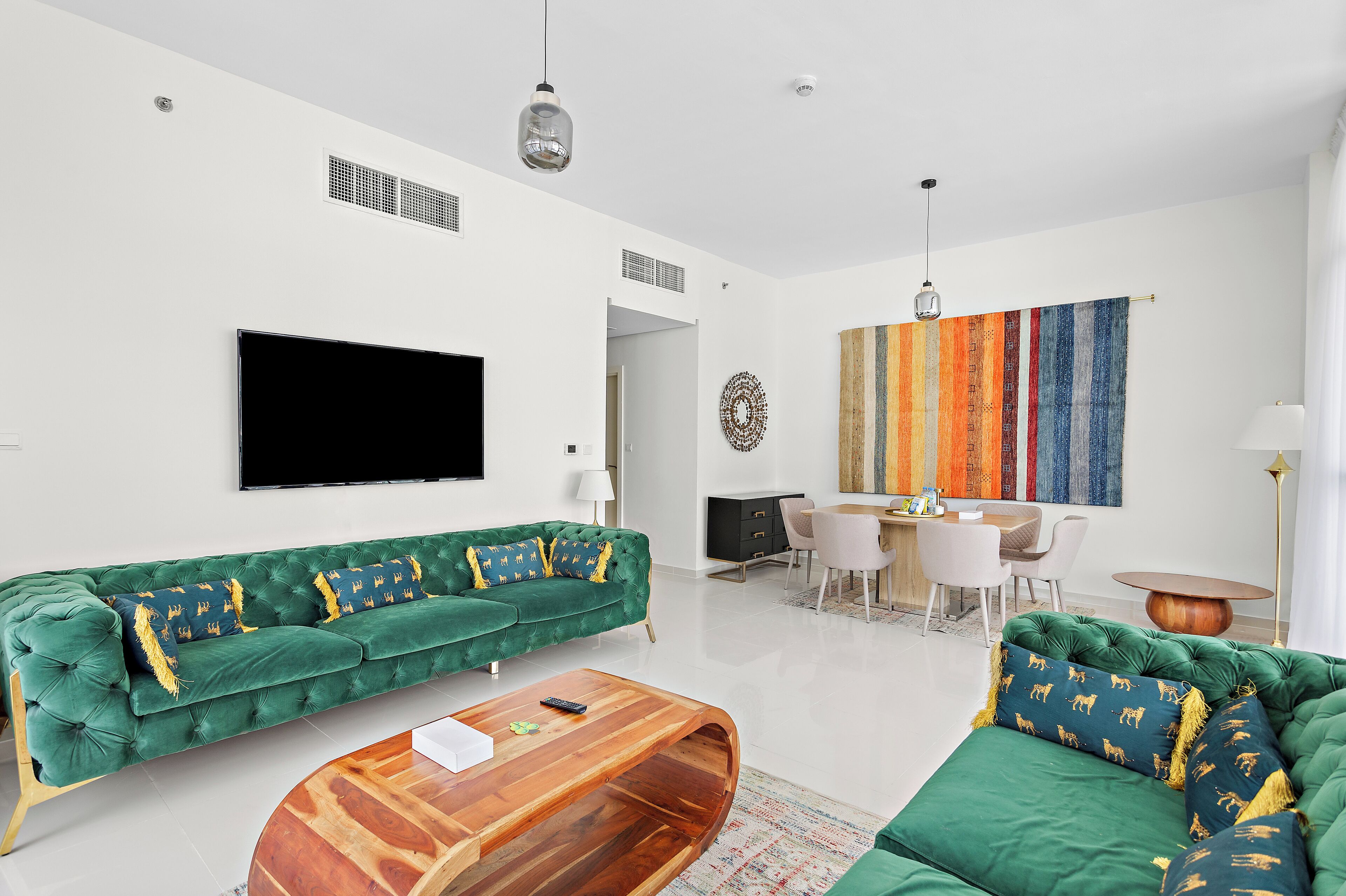 A modern living room with a green sofa set, a wooden coffee table, and a flat-screen TV mounted on the wall.